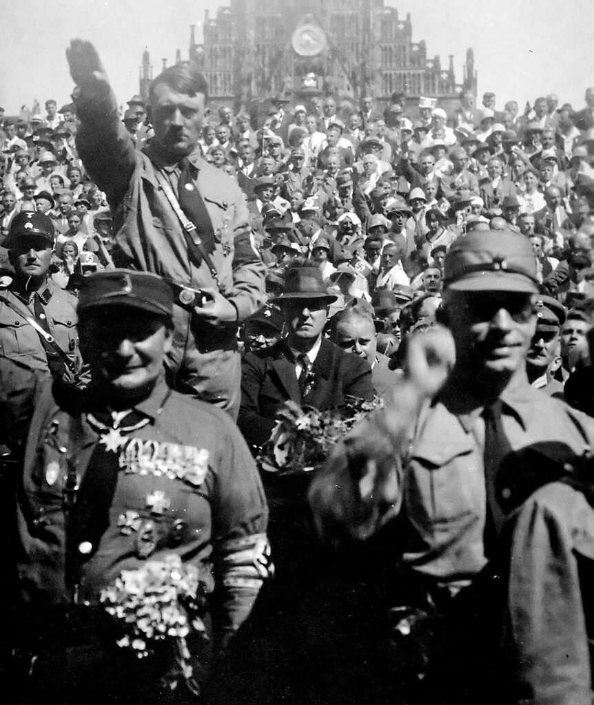 Hitler posa com uma saudação nazista em Nuremberg com membros da SA em 1928. À sua esquerda está Julius Streicher, e abaixo dele está Hermann Göring antes da Noite das Facas Longas
